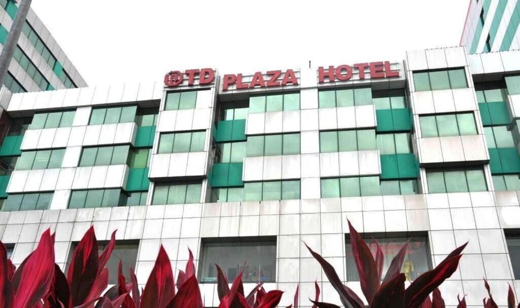 a hotel building with red plants in front of it at TD Plaza Hotel in Kota Kinabalu