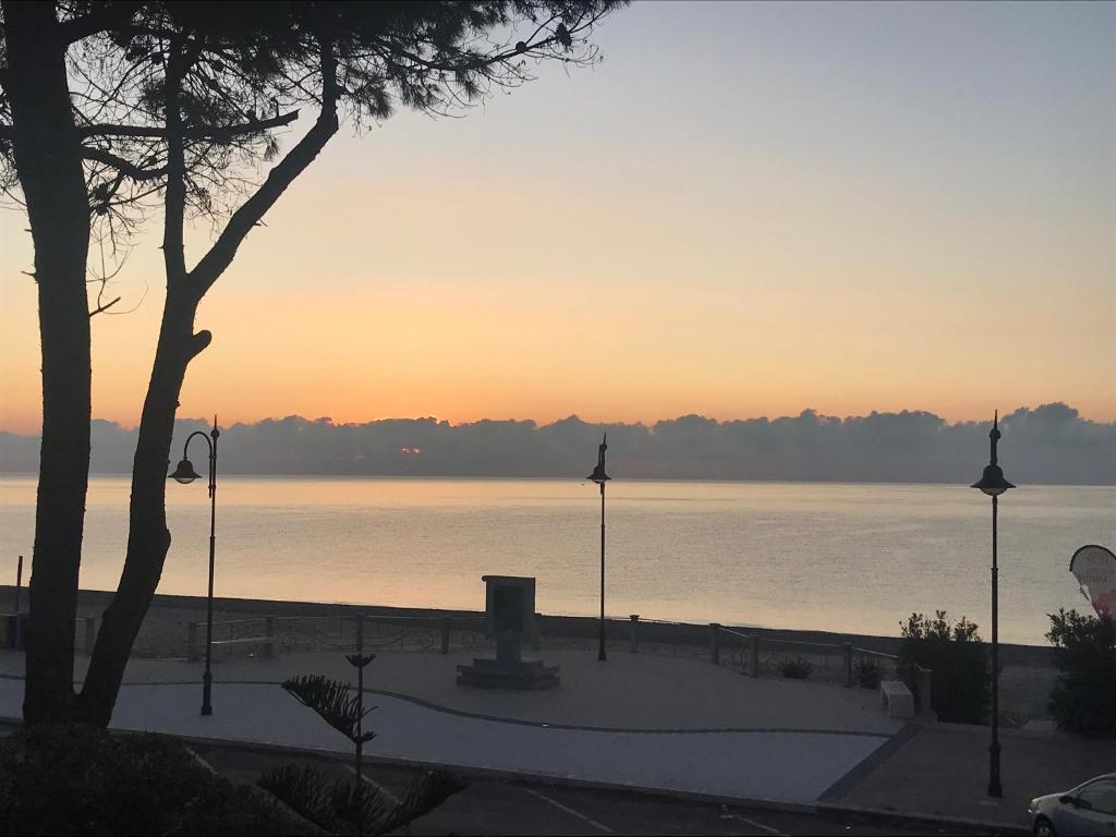 una puesta de sol sobre un cuerpo de agua con un árbol en Terrazza sul mare - Villa Tota -, en Ardore Marina