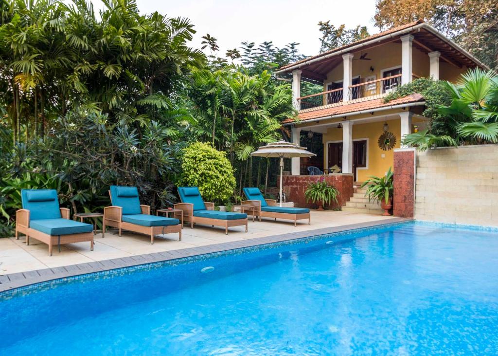 a villa with a swimming pool and chairs and a house at Serendipity House Goa in Nerul