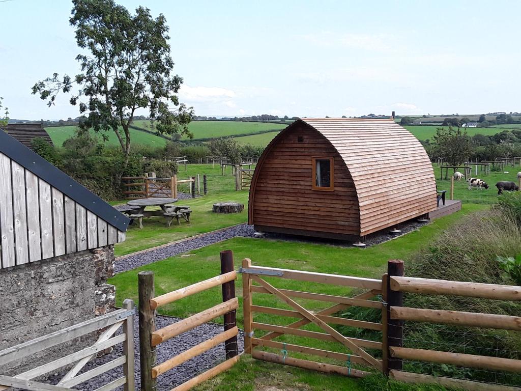 un granero de madera en un campo con una valla en Larkworthy Farm Glamping Holiday Cabins, en Ashwater