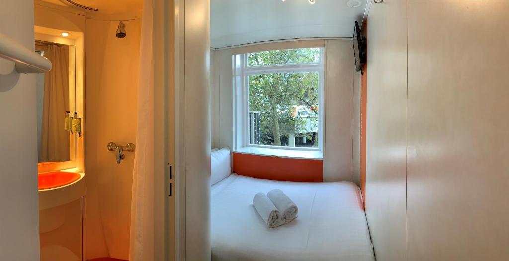 asiento junto a la ventana en una habitación pequeña con 2 toallas blancas en easyHotel South Kensington, en Londres