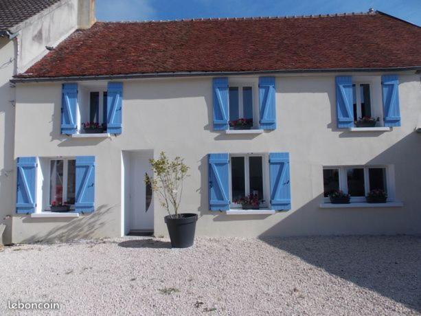 uma casa branca com persianas azuis e uma árvore em frente em Le gîte du bois sebille em Verdelot