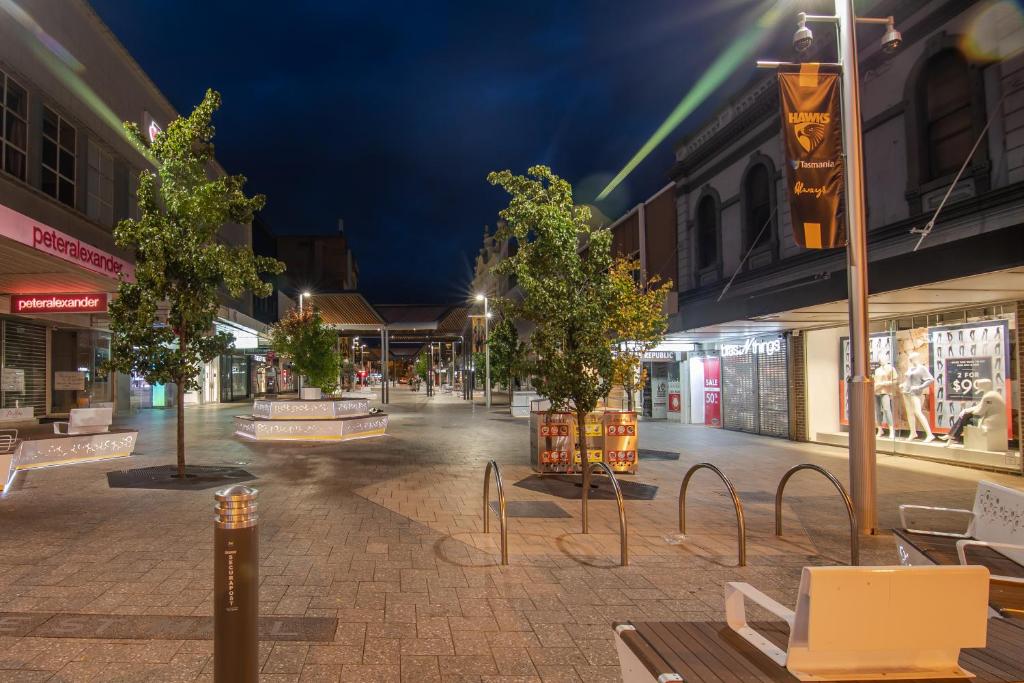 una strada vuota di notte con alberi e panchine di Central city apartment a Launceston