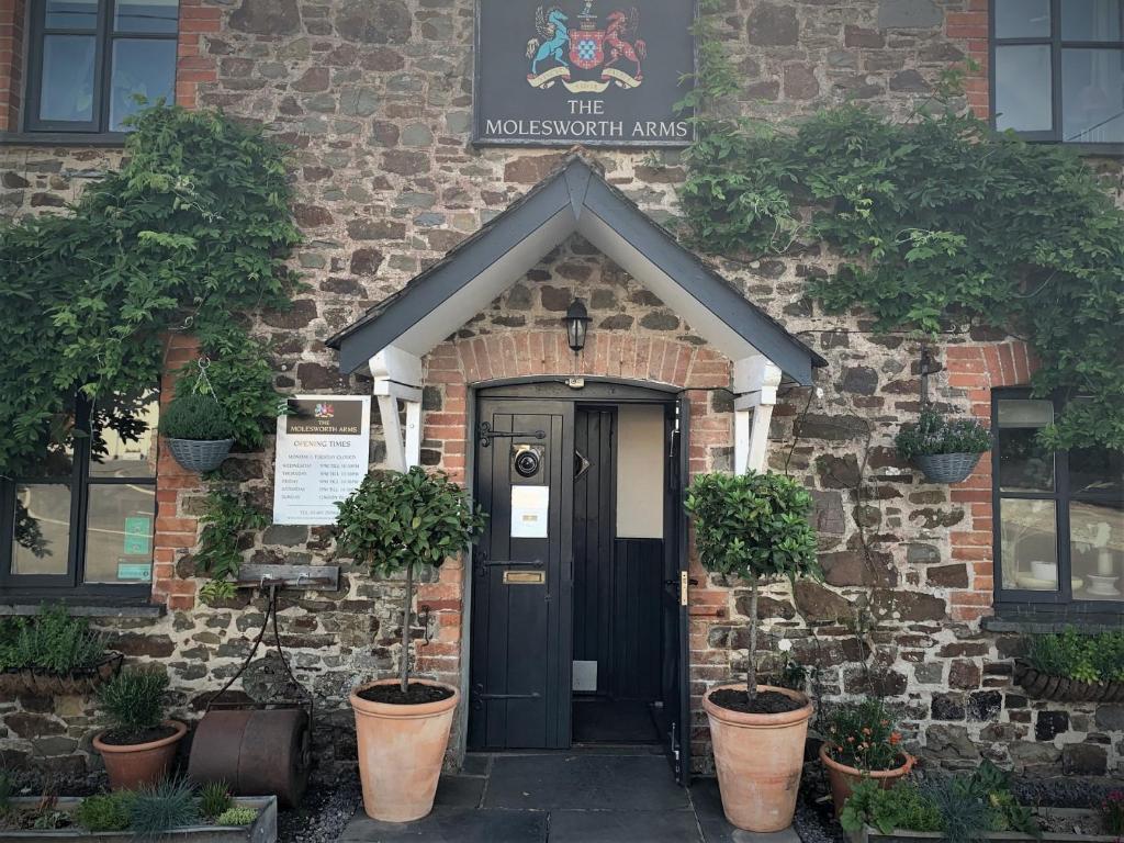 uma porta da frente de um edifício de tijolos com vasos de plantas em Molesworth Arms Pyworthy em Holsworthy