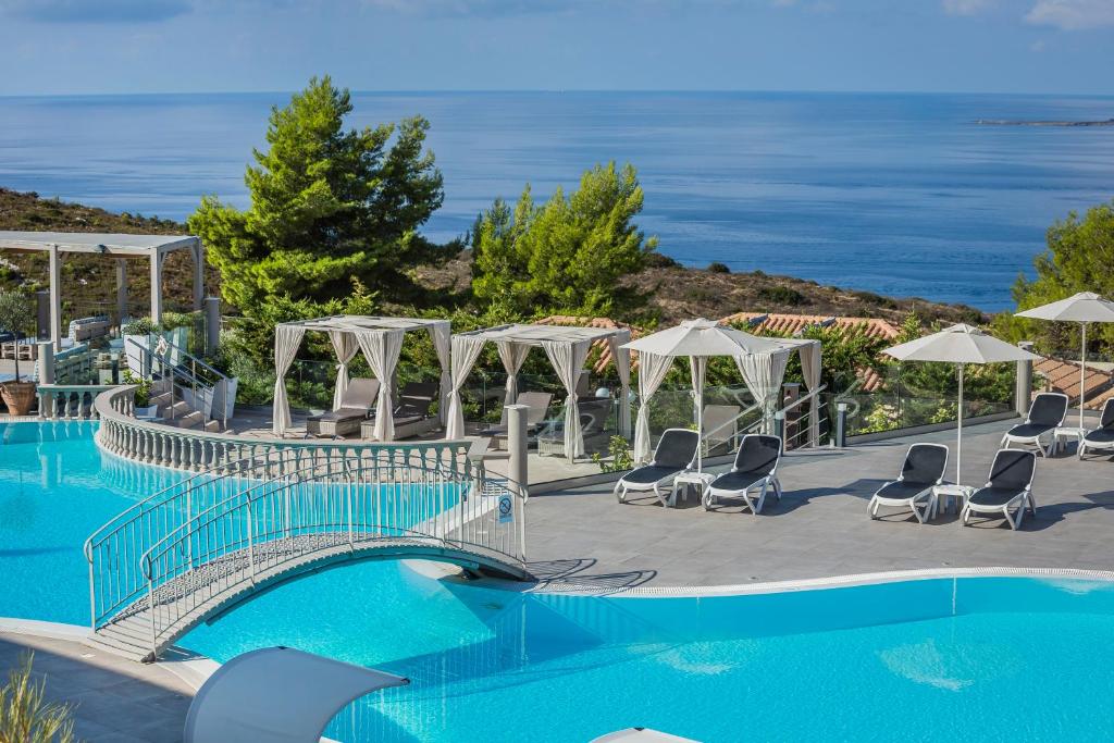 una piscina con un puente y sillas y el océano en Dionysos Village Resort en Lassi