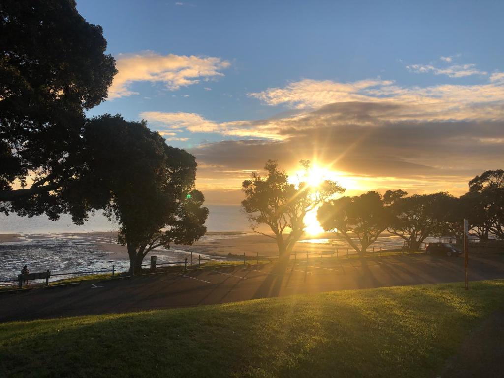 um pôr-do-sol sobre uma praia com árvores e o oceano em Central Howick Uxbridge Apartments em Auckland