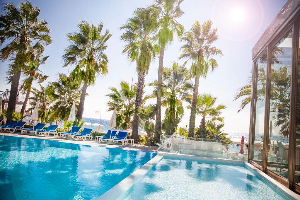 a swimming pool with palm trees and the ocean at Hotel Caravelle Thalasso & Wellness in Diano Marina