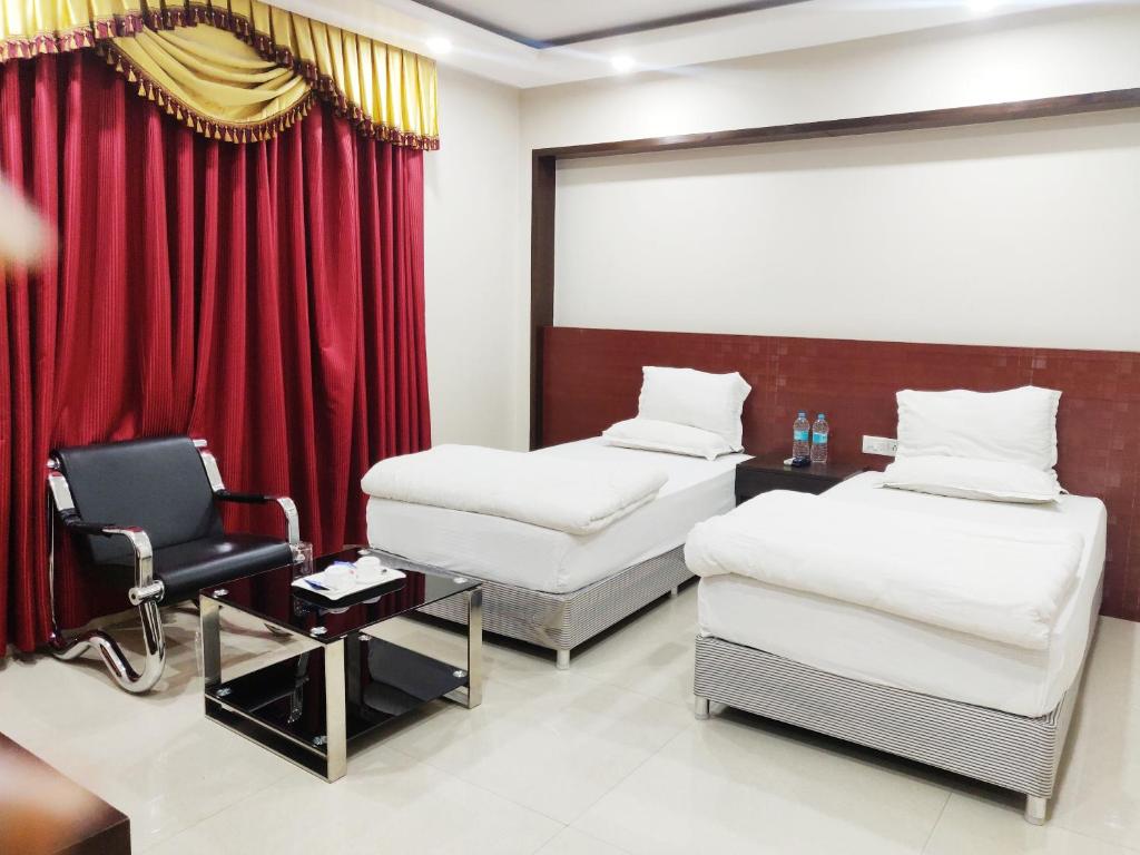 um quarto de hotel com duas camas e uma cadeira em Bodhgaya Seven Inn Hotel n Restaurant em Bodh Gaya