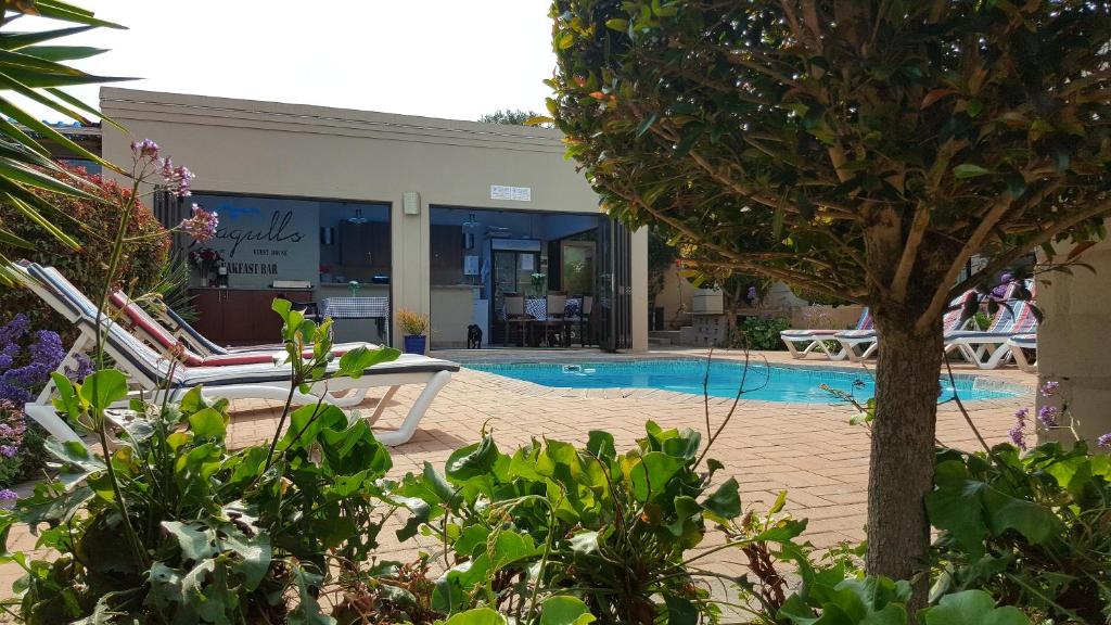 a swimming pool with two lawn chairs next to a building at Seagulls Guest House in Langebaan