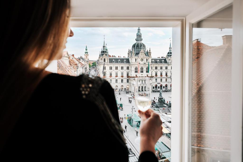 una mujer sosteniendo una copa de vino delante de una ventana en Kaiser Apartments - City Centre of Graz, en Graz