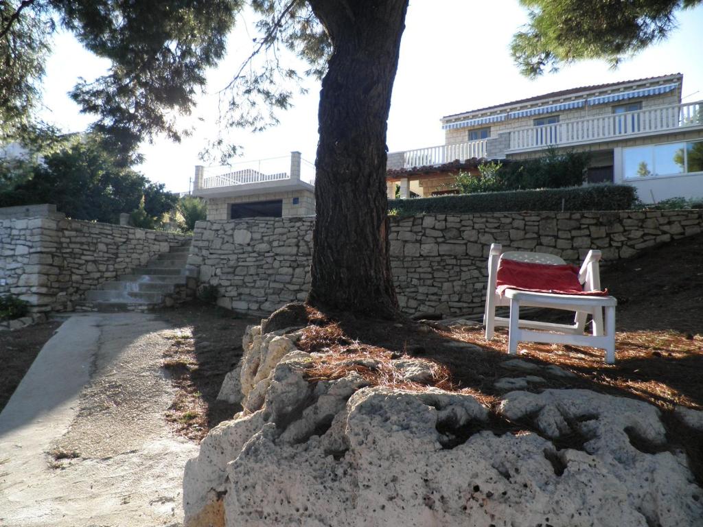 een witte stoel onder een boom naast een muur bij Apartments Holiday in Lumbarda