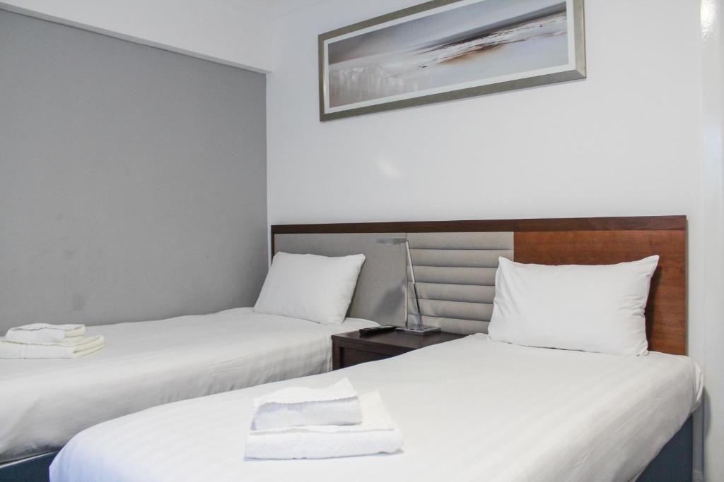 two beds in a room with white sheets at Heathrow Lodge in Hillingdon