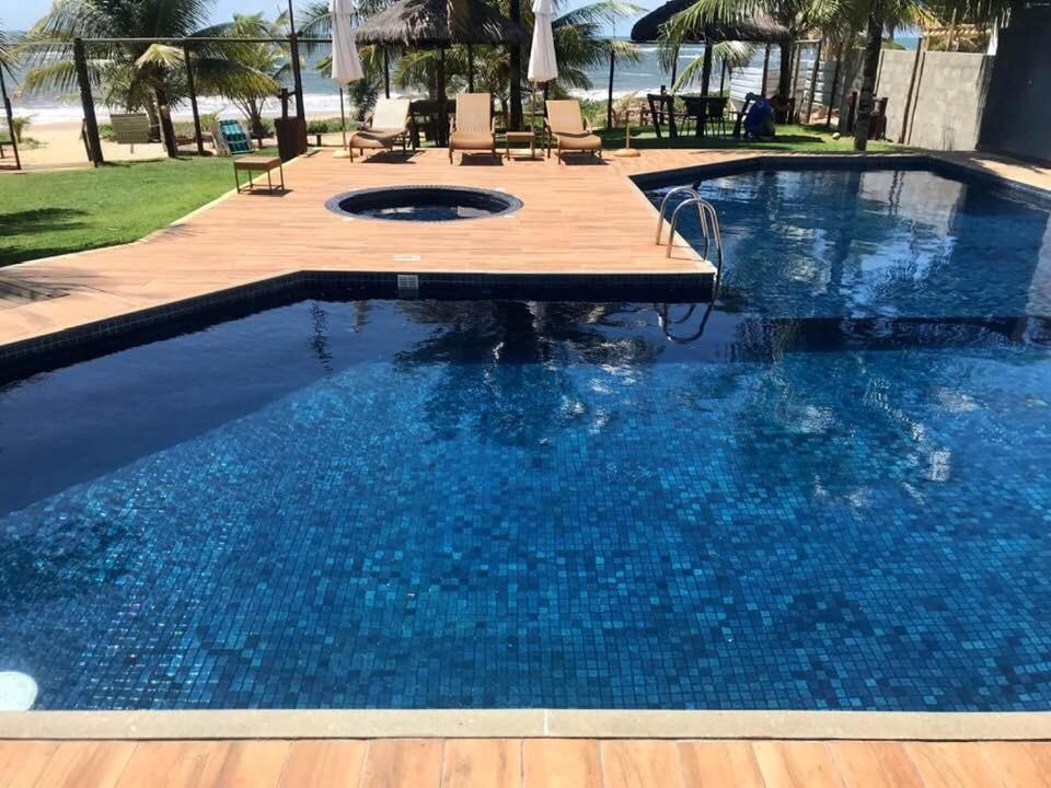 a swimming pool with a wooden deck and blue water at Village Praia de Itacimirim in Itacimirim