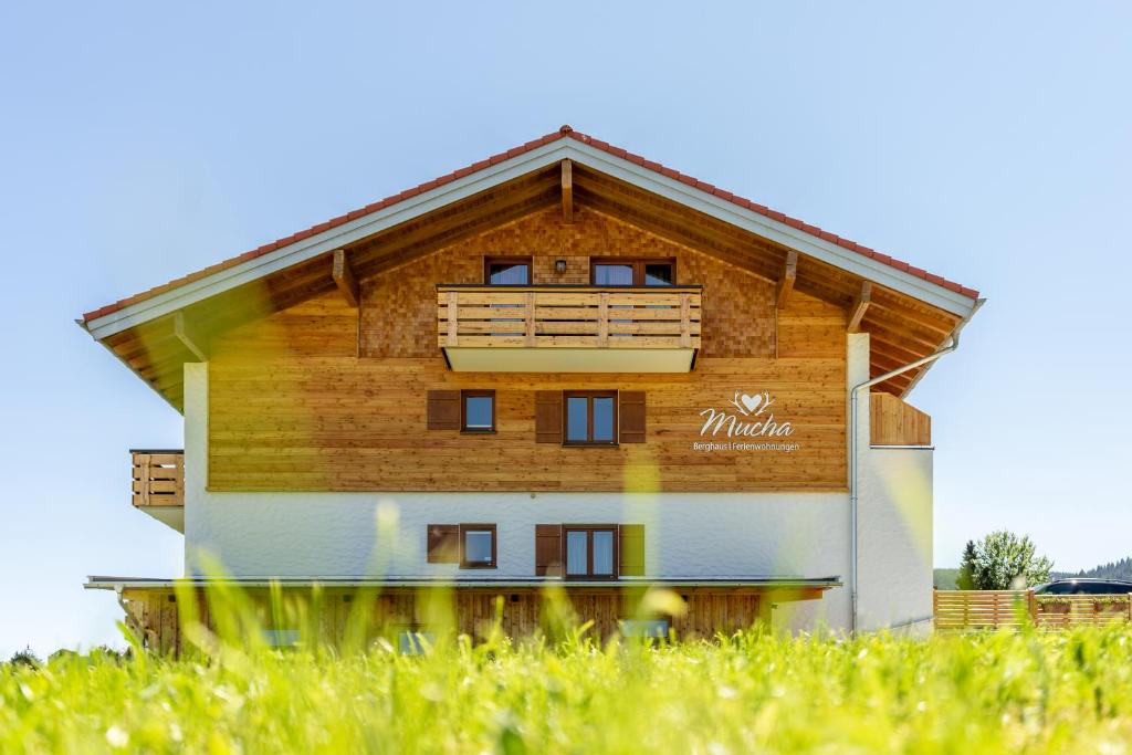 un edificio de madera con balcón en un campo de césped en Berghaus Mucha - Ferienwohnungen - Naturpark Partner en Bolsterlang