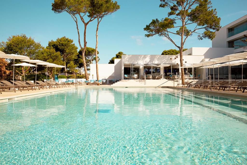 a large swimming pool with chairs and a building at Diamant Hotel & Aparthotel in Cala Ratjada