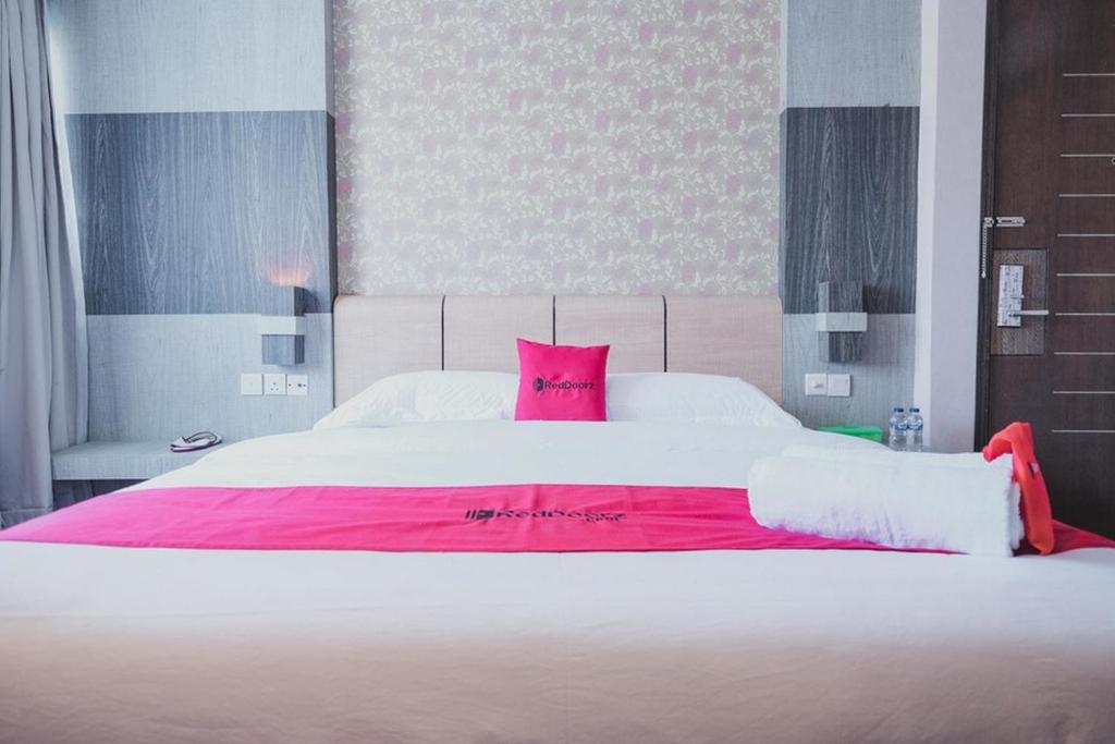 a large white bed with a pink blanket on it at RedDoorz Plus near Pantai Coastarina 2 Batam in Batam Center