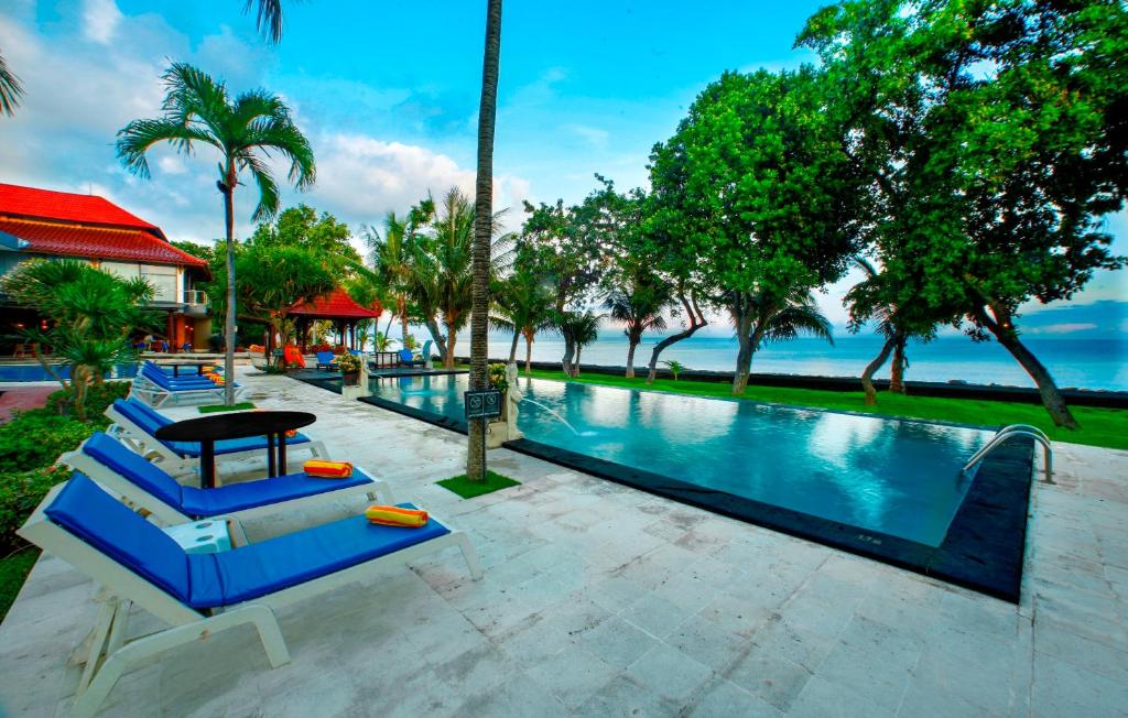 a swimming pool with blue lounge chairs and the ocean at Puri Saron Hotel Baruna Beach Lovina in Lovina