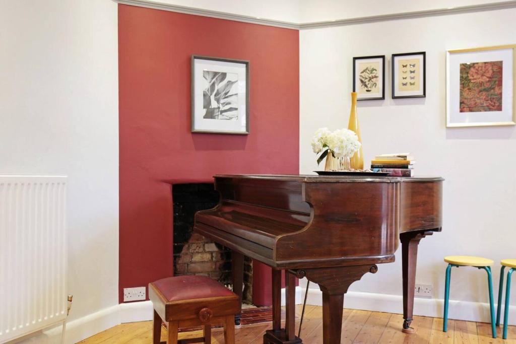 a piano in a living room with a red wall at The Majestic Oxford House - Piano - Garden in Oxford