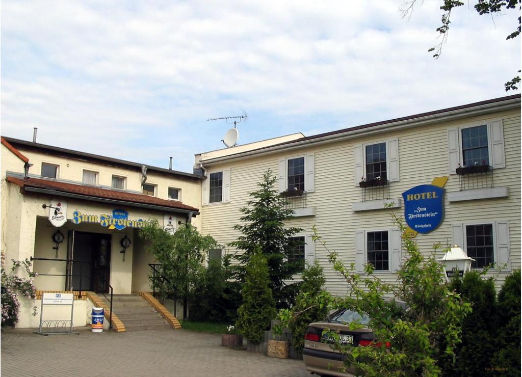 a white building with a blue sign in front of it at Hotel & Restaurant "Zum Firstenstein" in Königshain