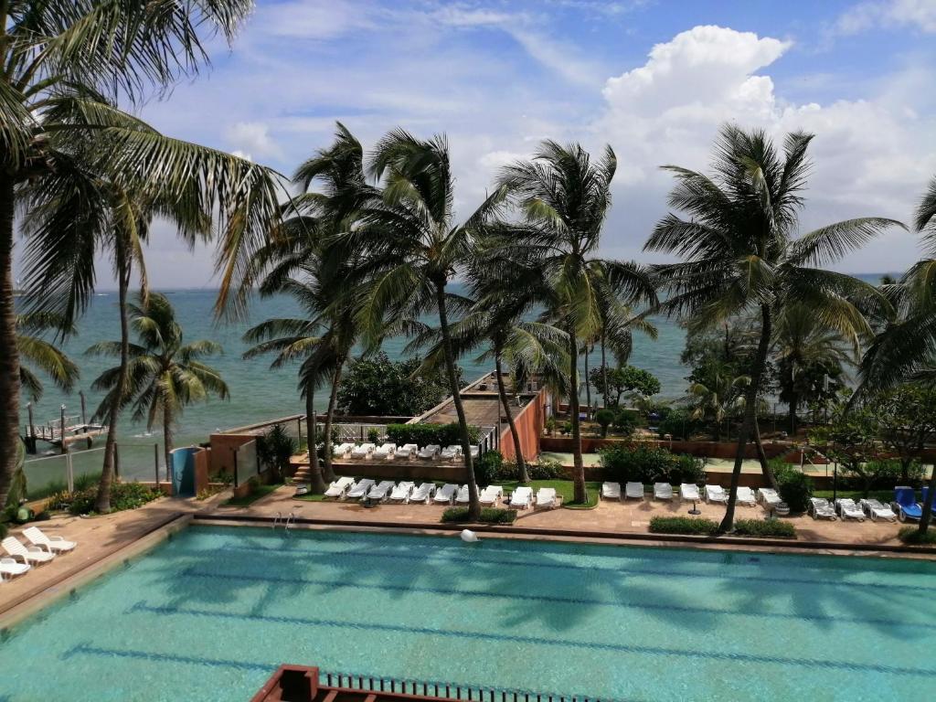 einen Pool mit Palmen und dem Meer im Hintergrund in der Unterkunft Hotel Jardin Savana Dakar in Dakar