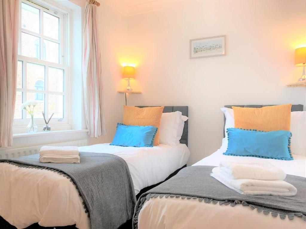 zwei Betten in einem Zimmer mit blauen und orangefarbenen Kissen in der Unterkunft Seaside Cottage with Parking in Worthing