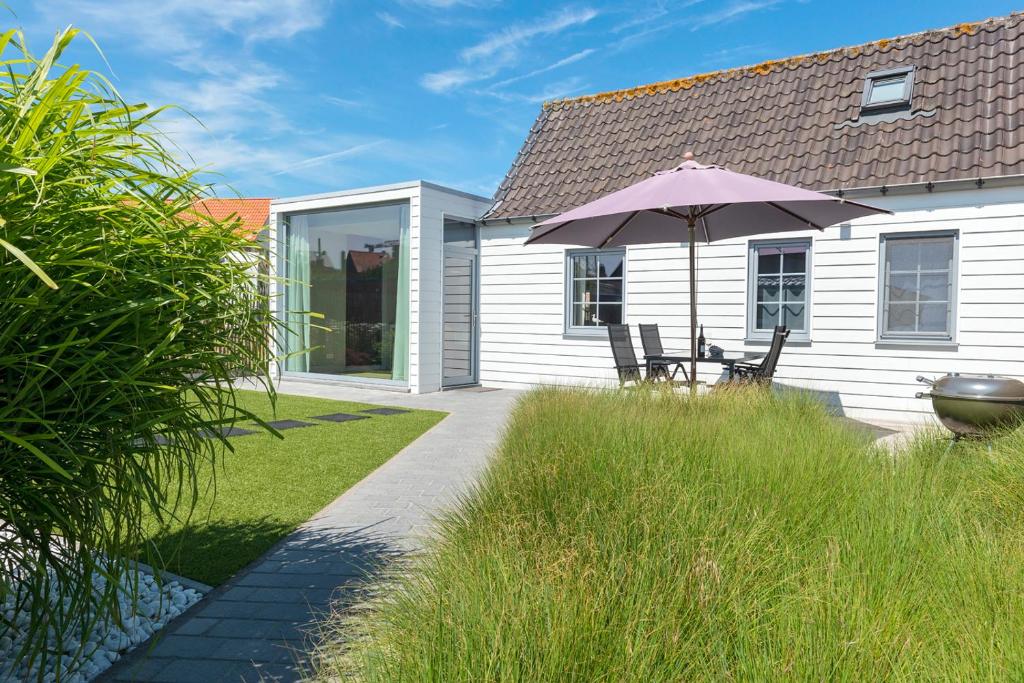 a house with a patio with an umbrella and chairs at Holiday Home Garnaalhuisje in Oostduinkerke
