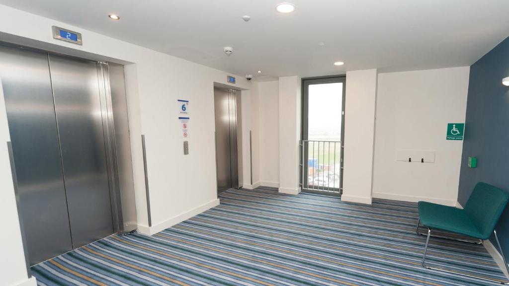 an empty hallway in an office with a green chair at Holiday Inn Express Aberdeen Airport by IHG in Dyce