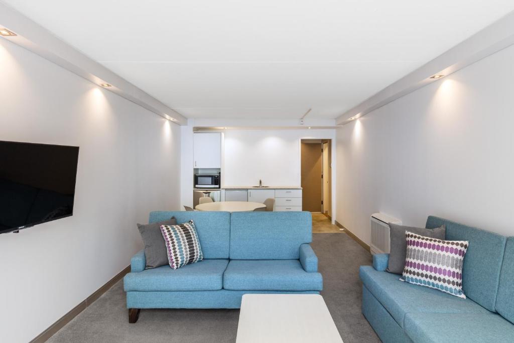 a living room with two blue couches and a tv at Holiday Inn Auckland Airport by IHG in Auckland