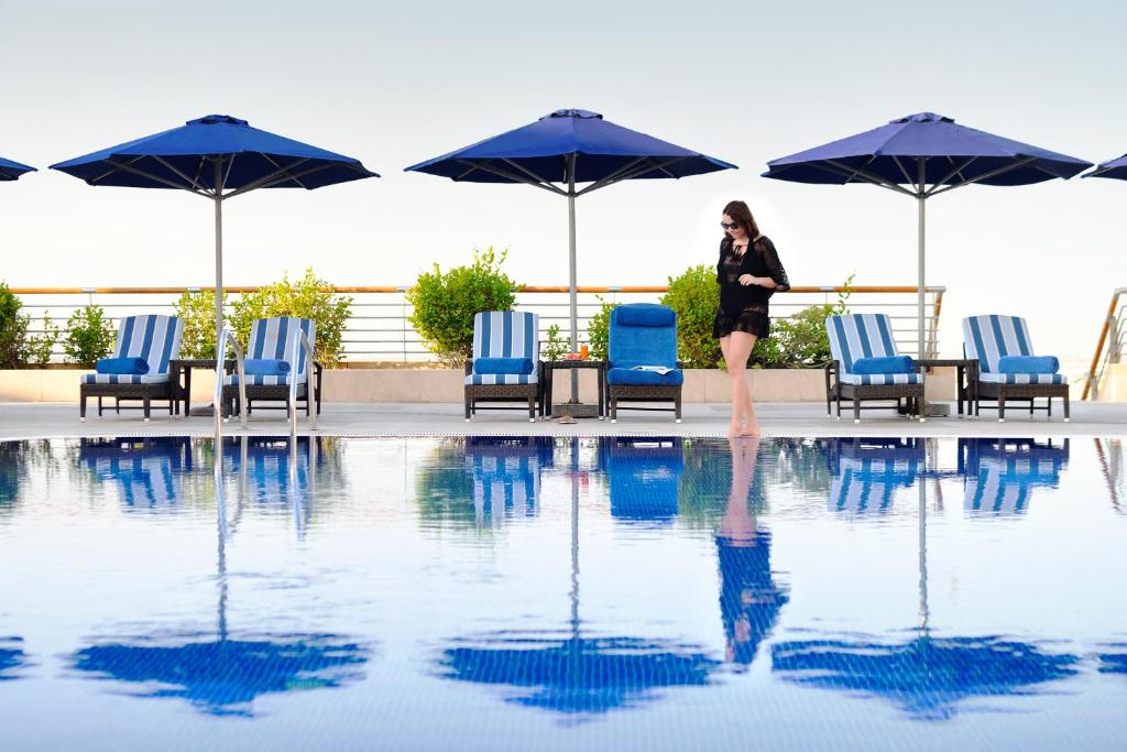 a woman standing next to a pool with chairs and umbrellas at InterContinental Abu Dhabi, an IHG Hotel in Abu Dhabi