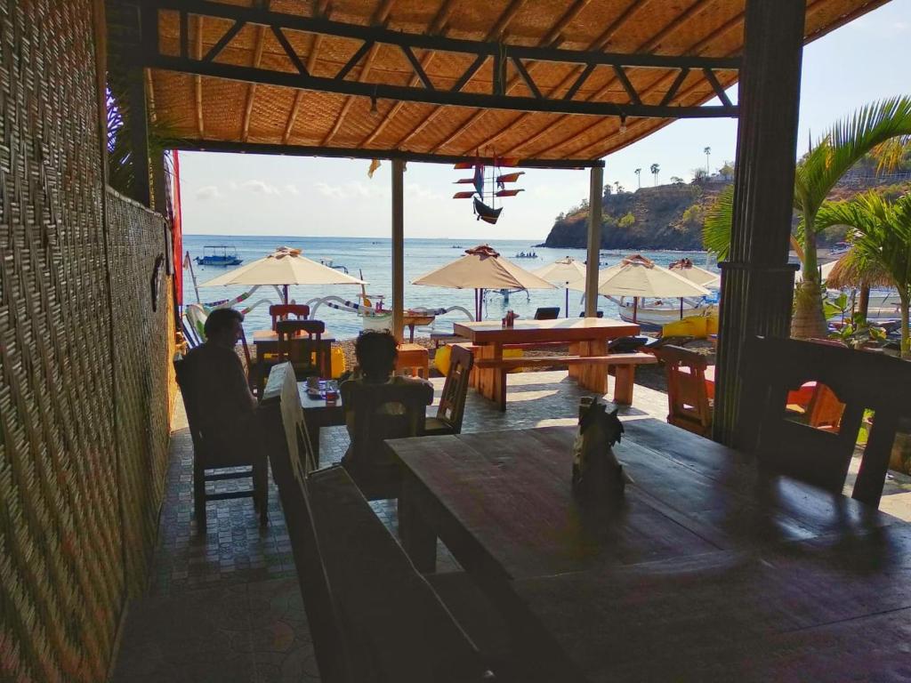 a restaurant with a view of the beach with tables and umbrellas at COCONUT BEACH BUNGALOWs & WARUNG in Amed