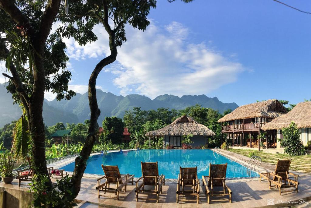 a resort pool with chairs and mountains in the background at Mai Chau Sky Resort in Mai Chau