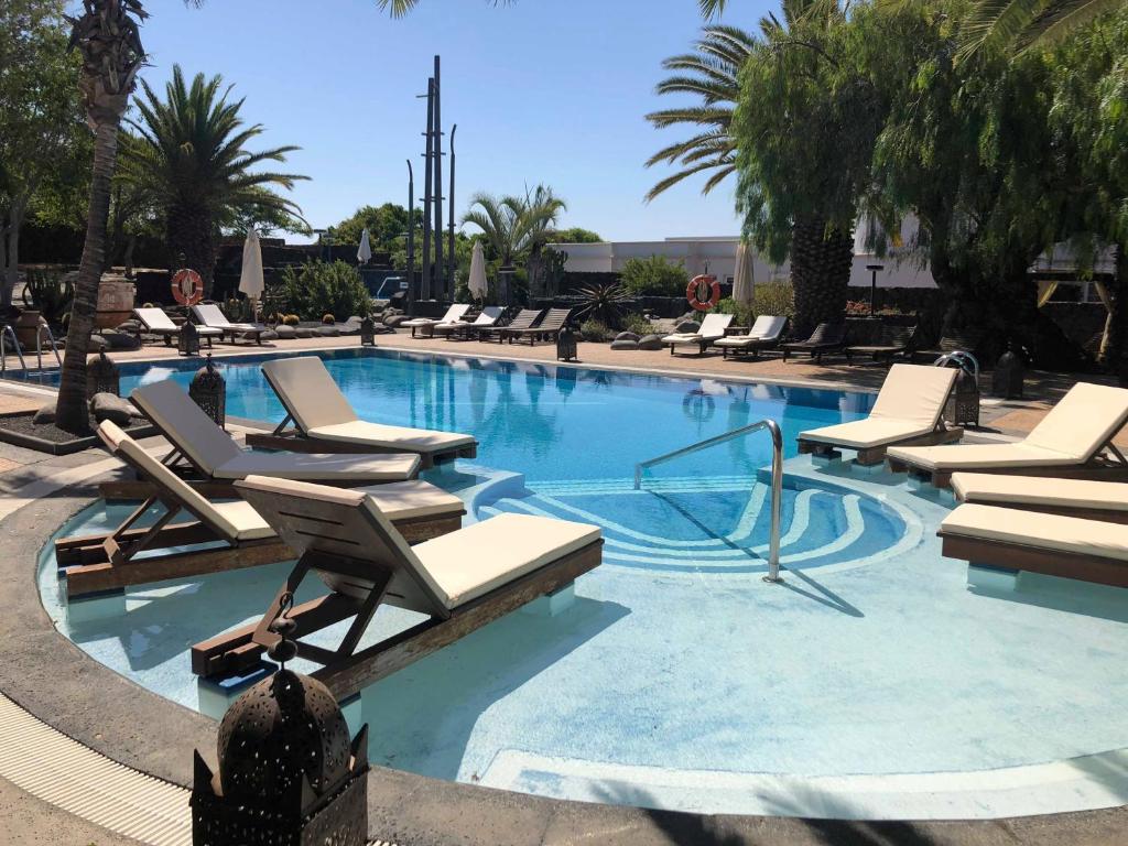 a large swimming pool with lounge chairs and palm trees at Villa VIK - Hotel Boutique in Arrecife