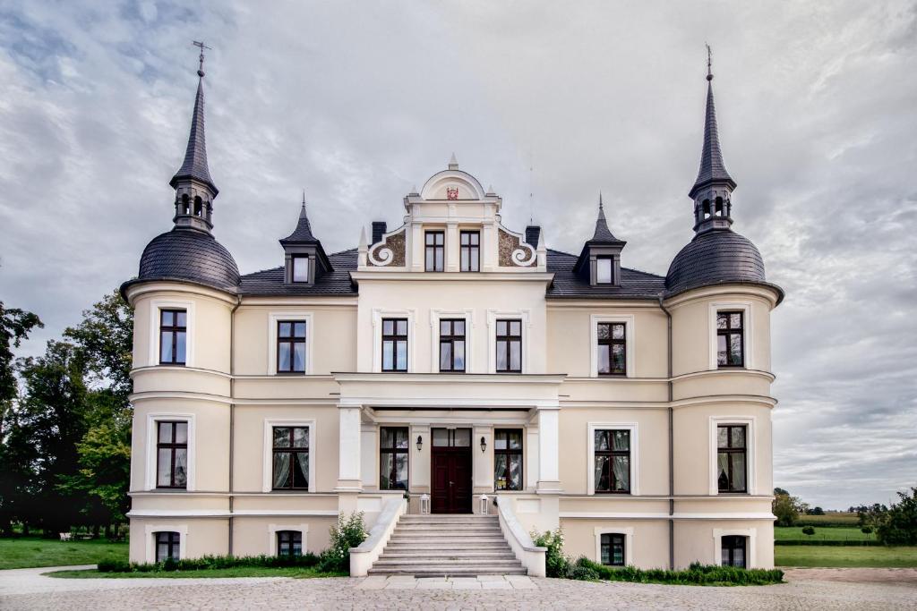 une grande maison blanche avec deux tours en haut dans l'établissement Pałac w Orli - pokoje, restauracja, à Koźmin