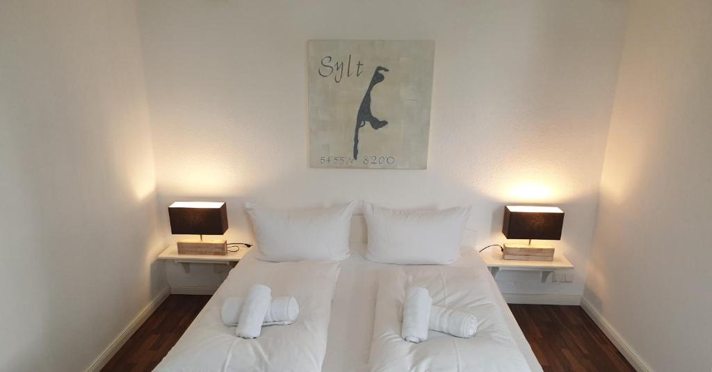 a bedroom with a bed with white sheets and two lamps at Haus Bomhoff Sylt in Westerland