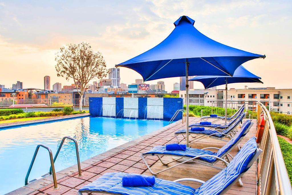 a group of lounge chairs with an umbrella next to a pool at RH Hotel Pretoria in Pretoria