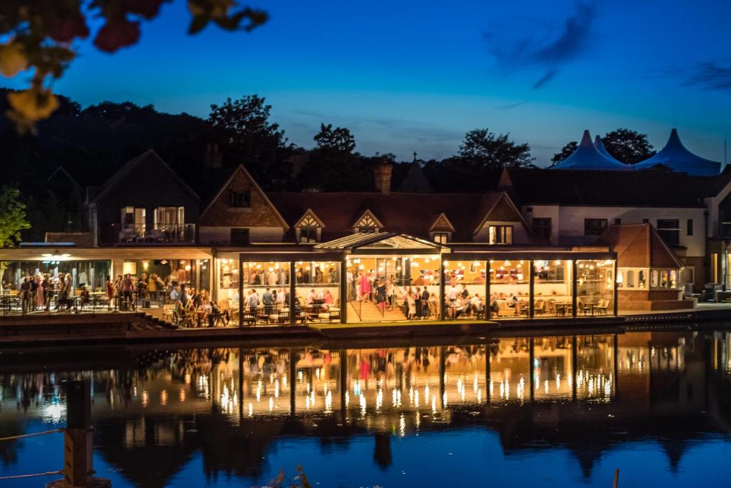 a building lit up at night next to a body of water at The Swan, Streatley, Berkshire in Streatley