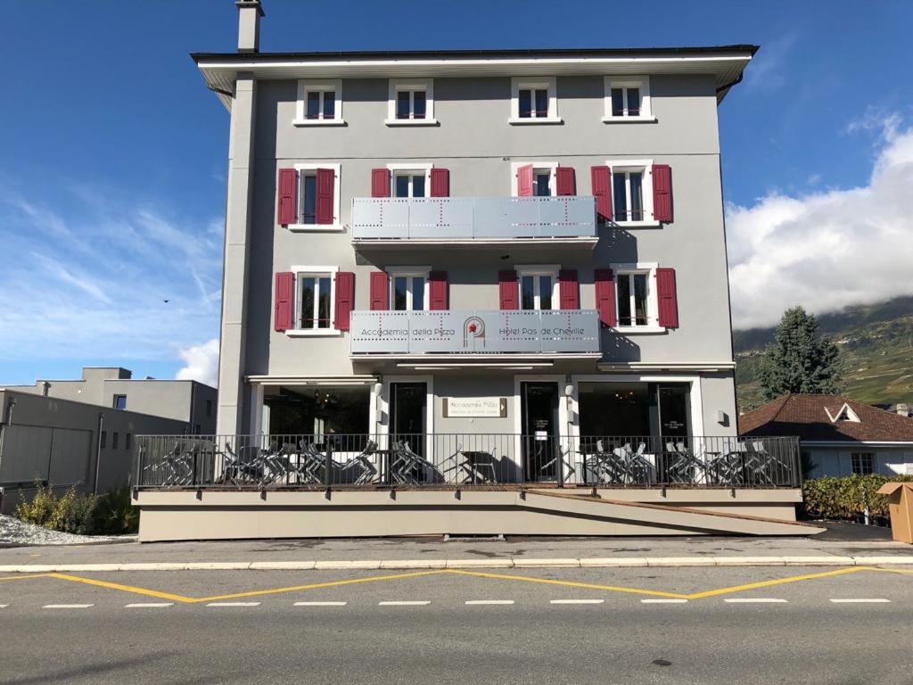 Gran edificio blanco con ventanas rojas y balcón. en Hotel pas de Cheville en Conthey