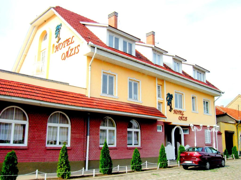 a red and yellow building with a car parked in front at Oázis Hotel Étterem in Kiskunfélegyháza