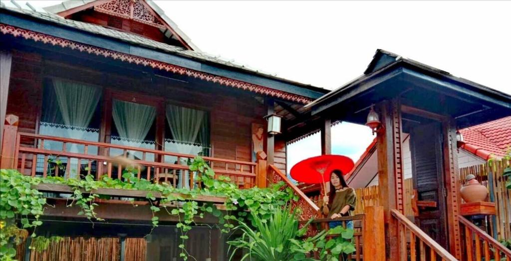 a woman standing on the balcony of a house with a red umbrella at Lampang Lanna Home in Lampang