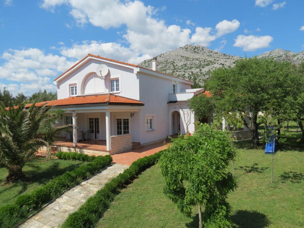 biały dom z ogrodem i górami w tle w obiekcie Apartments Villa Andreja w mieście Starigrad-Paklenica