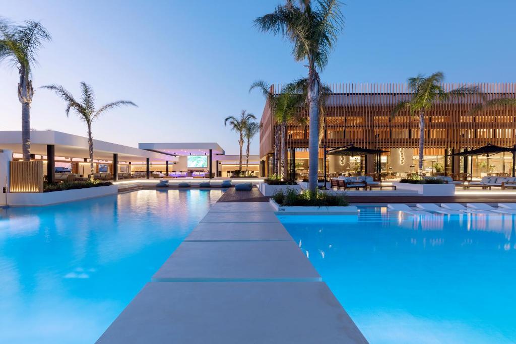 a swimming pool with palm trees in front of a building at D' Andrea Lagoon All Suites - Adults Only in Marmari