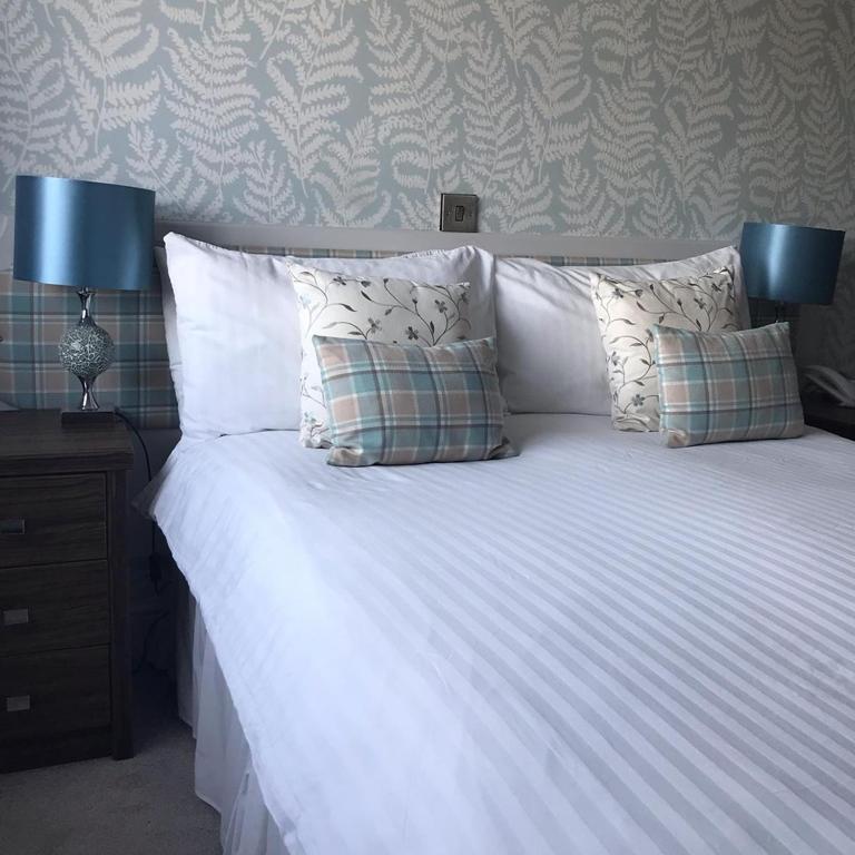 a white bed with pillows and two lamps on a table at The Pines Hotel in Swanage