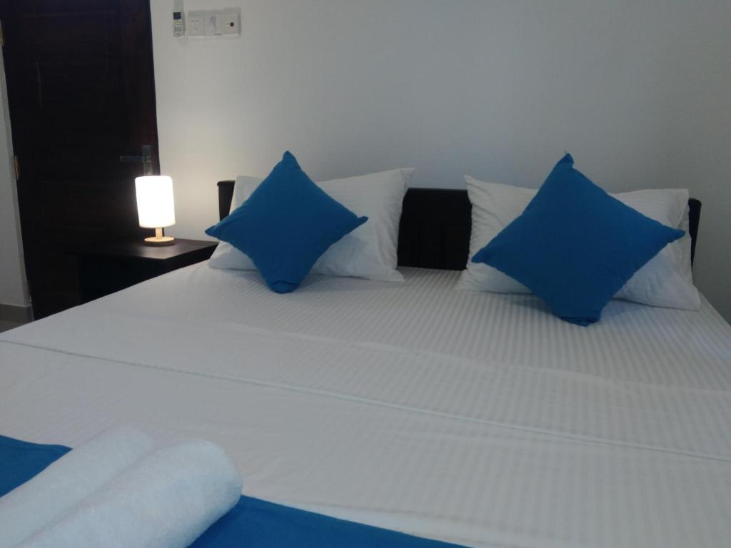 a large white bed with blue pillows and a lamp at Queens Airport Residence in Negombo