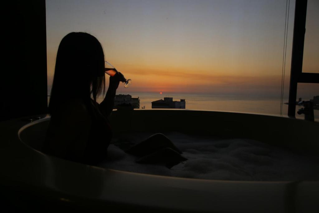 فندق سانريز في جونية: امرأة جالسة في حوض الاستحمام تشاهد غروب الشمس