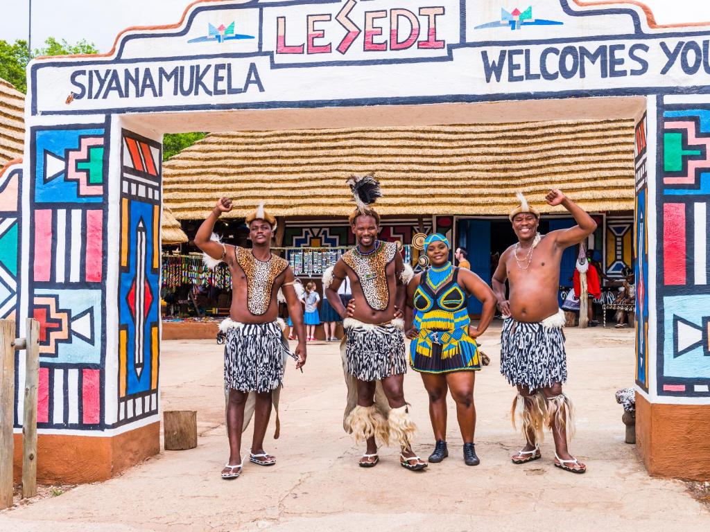 un grupo de hombres con sus perros delante de una puerta en aha Lesedi African Lodge & Cultural Village, en Pelindaba