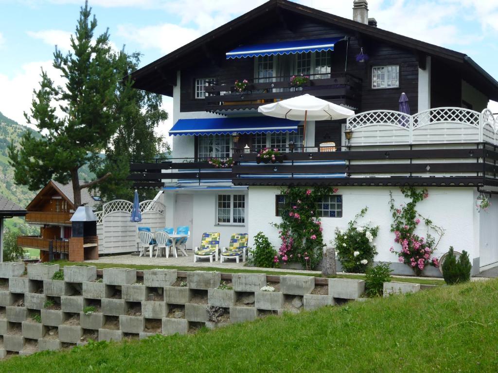 Casa blanca con sombrilla, mesas y sillas en Haus Edelweiss, en Grächen