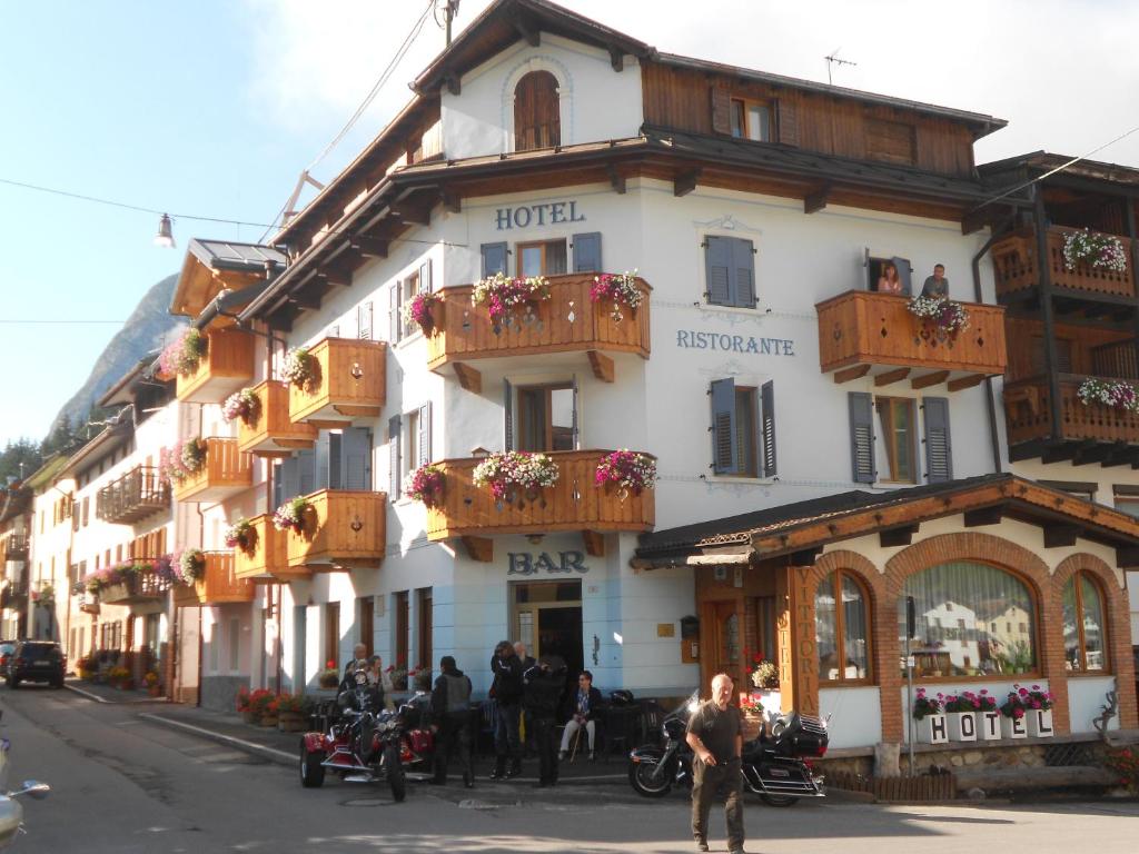 um grande edifício branco com varandas de madeira numa rua em Albergo Vittoria em Santo Stefano di Cadore