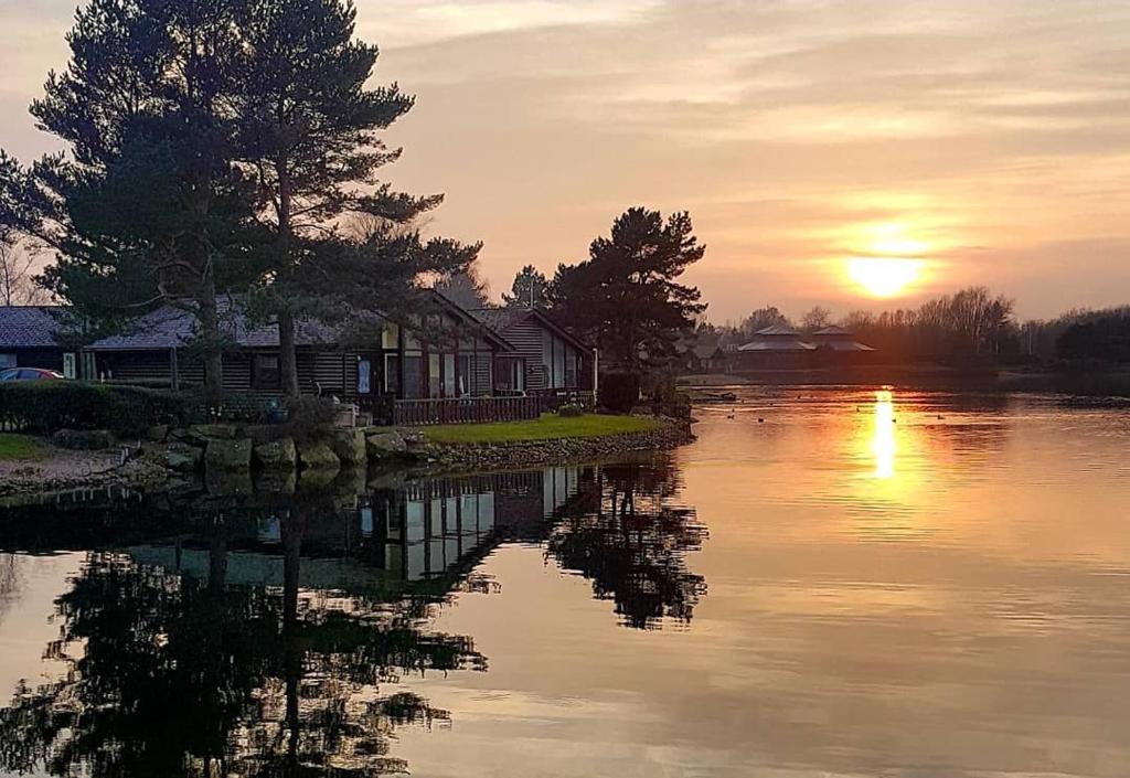 een zonsondergang over een rivier met een huis en bomen bij Keer lodge - Pine Lake Resort in Carnforth