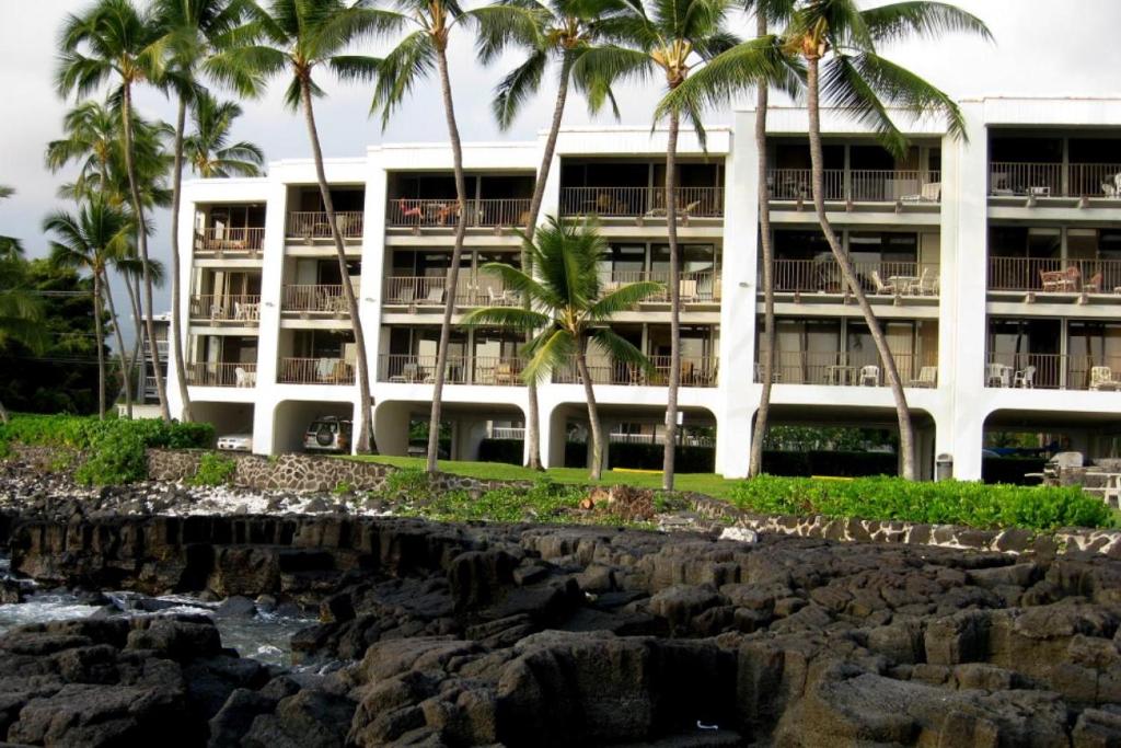 ein Gebäude mit Palmen vor einem Wasserkörper in der Unterkunft Oceanfront-Incredible Views, Surf Break & Romantic Sunsets at Bali Kai 223 in Kailua-Kona