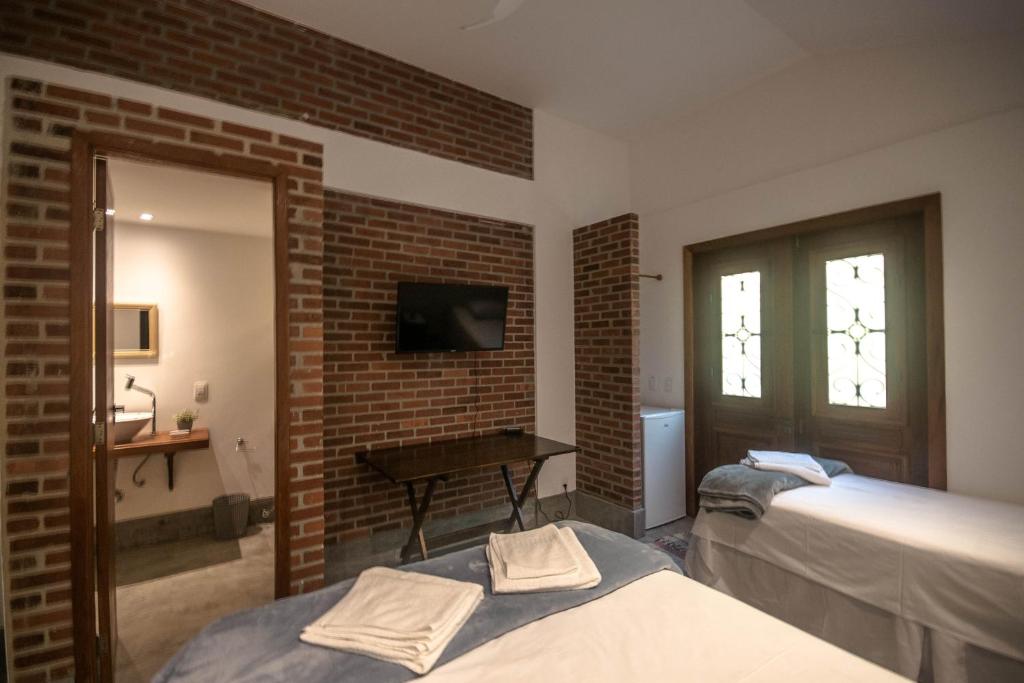 a bedroom with two beds and a television and a brick wall at Casa Flor Paquetá in Paquetá